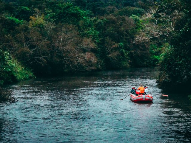 Red inflatable raft with paddlers on a calm river between dense jungle