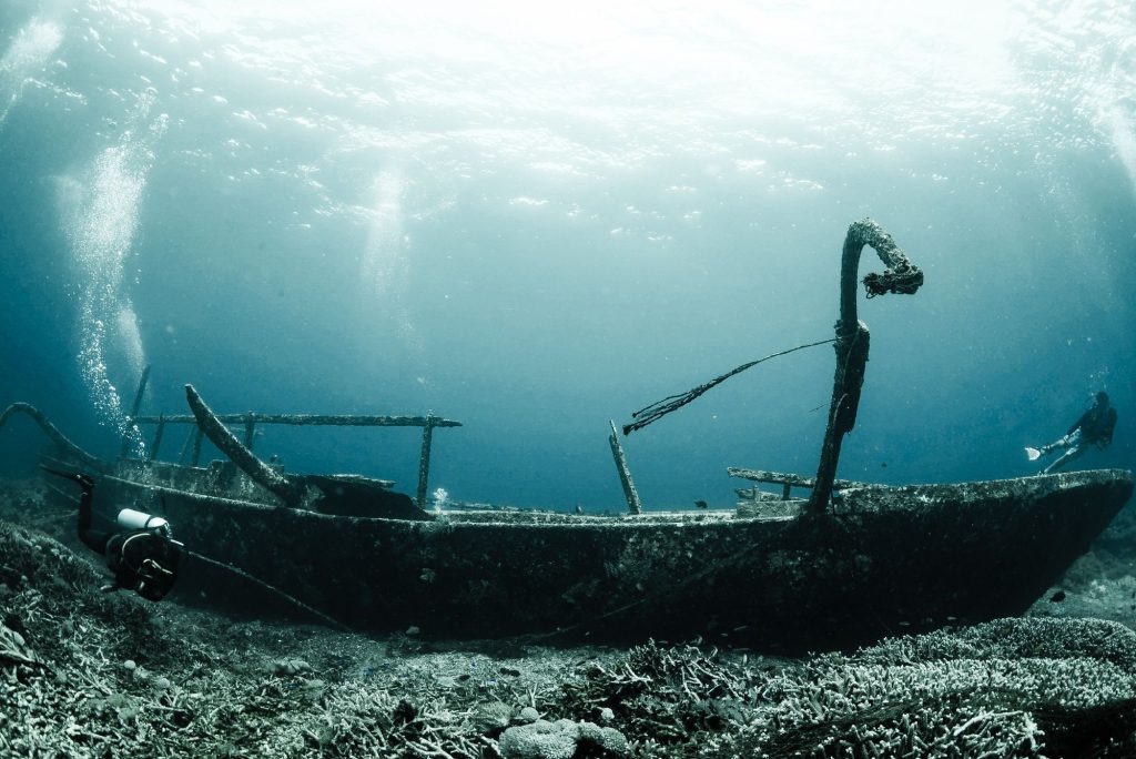 Sunken wooden shipwreck underwater with divers and light rays from the surface