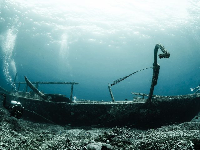 Sunken wooden shipwreck underwater with divers and light rays from the surface