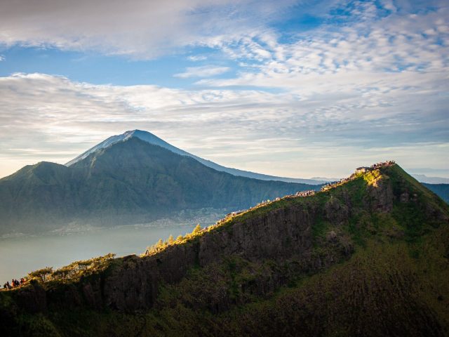 Mount Batur ridge with trekkers along the rim and Mount Agung behind, under sunrise clouds