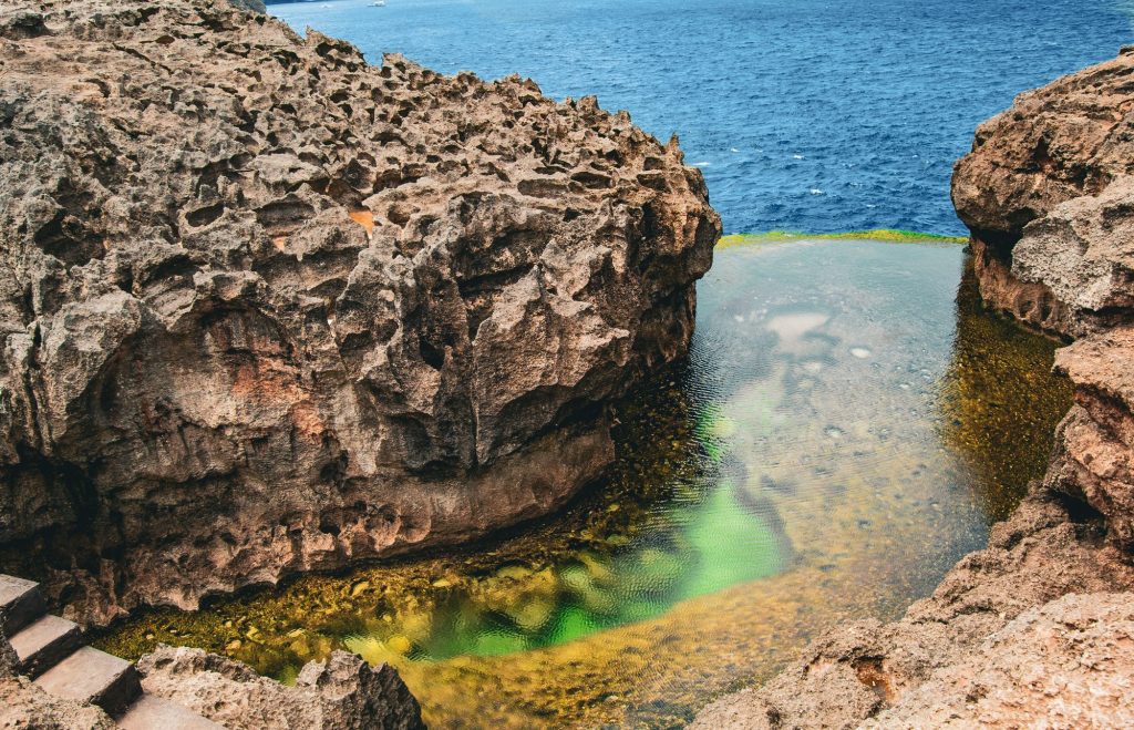 Rocky cliffs and the green natural rock pool of Angel's Billabong above the blue sea, Nusa Penida