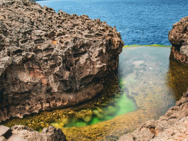 Rocky cliffs and the green natural rock pool of Angel's Billabong above the blue sea, Nusa Penida