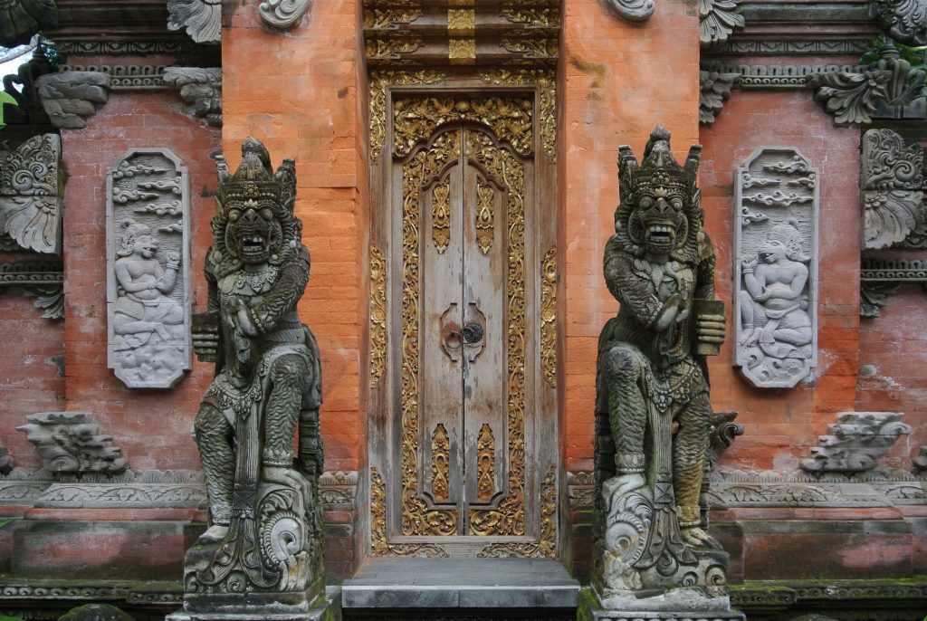 Ornate carved brick and gold-leaf entrance of a Balinese temple in Ubud, flanked by two guardian statues