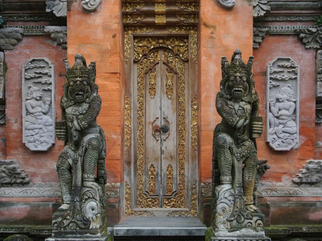 Ornate carved brick and gold-leaf entrance of a Balinese temple in Ubud, flanked by two guardian statues