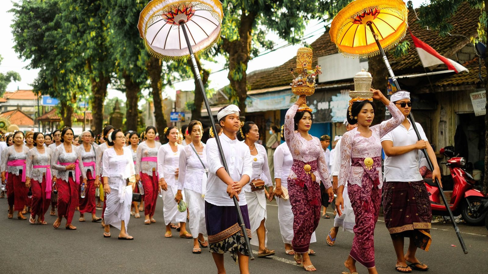 Procession of Balinese women and men in kebaya, sarong and white, with umbrellas and offerings on heads