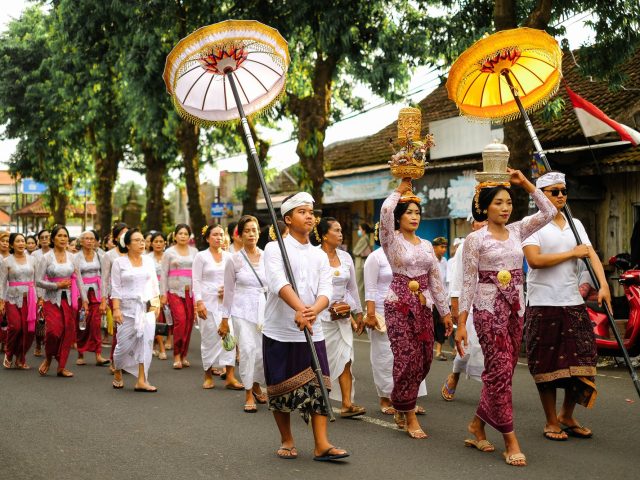 Procession of Balinese women and men in kebaya, sarong and white, with umbrellas and offerings on heads